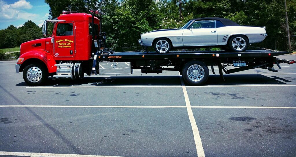 A red flatbed tow truck from Rubber Chicken Towing LLC towing a classic white convertible car in Charlotte, NC.