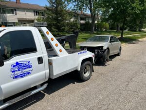 A white tow truck from ALDM Management towing a damaged silver car on a residential street in Cleveland, OH.