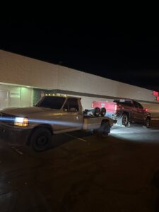 A tow truck from Henderson Towing & Recovery LLC towing a dark grey Ford Escape SUV in a parking lot in Denver, CO.