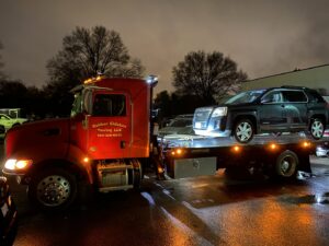 A red flatbed tow truck from Rubber Chicken Towing LLC towing a dark SUV at night in Charlotte, NC.
