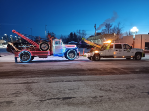 A Carnahan's Towing & Repair Inc. truck towing a decorated tow truck on a snowy road in Great Falls, MT.