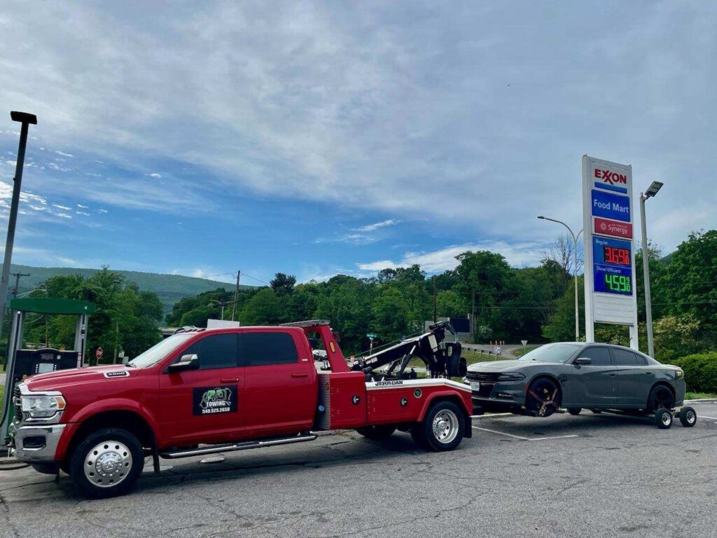 A red A and D Towing truck is towing a grey sedan from a gas station in Little Ferry, NJ.