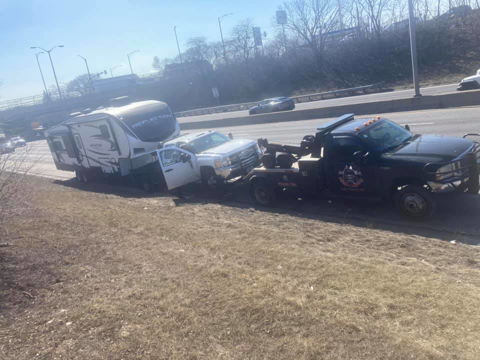 An O.T.W Towing & Recovery LLC tow truck towing a pickup truck and RV on a highway in Chicago, IL.