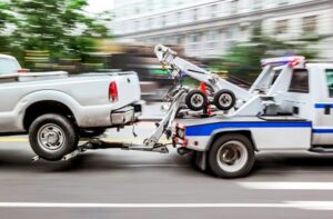 A tow truck from Emergency Towing Sacramento, CA, actively towing a white pickup truck on a city street.