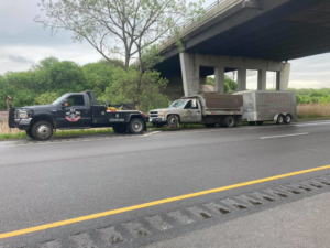 An O.T.W Towing & Recovery LLC tow truck towing a pickup truck and trailer on a highway in Chicago, IL.