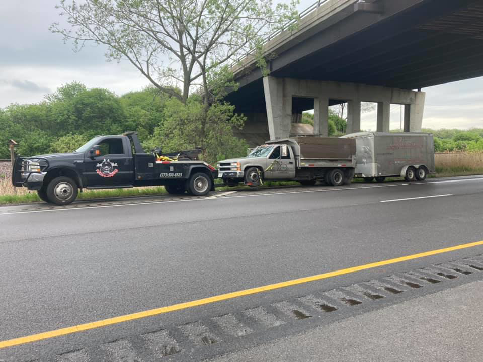 An O.T.W Towing & Recovery LLC tow truck towing a pickup truck and trailer on a highway in Chicago, IL.