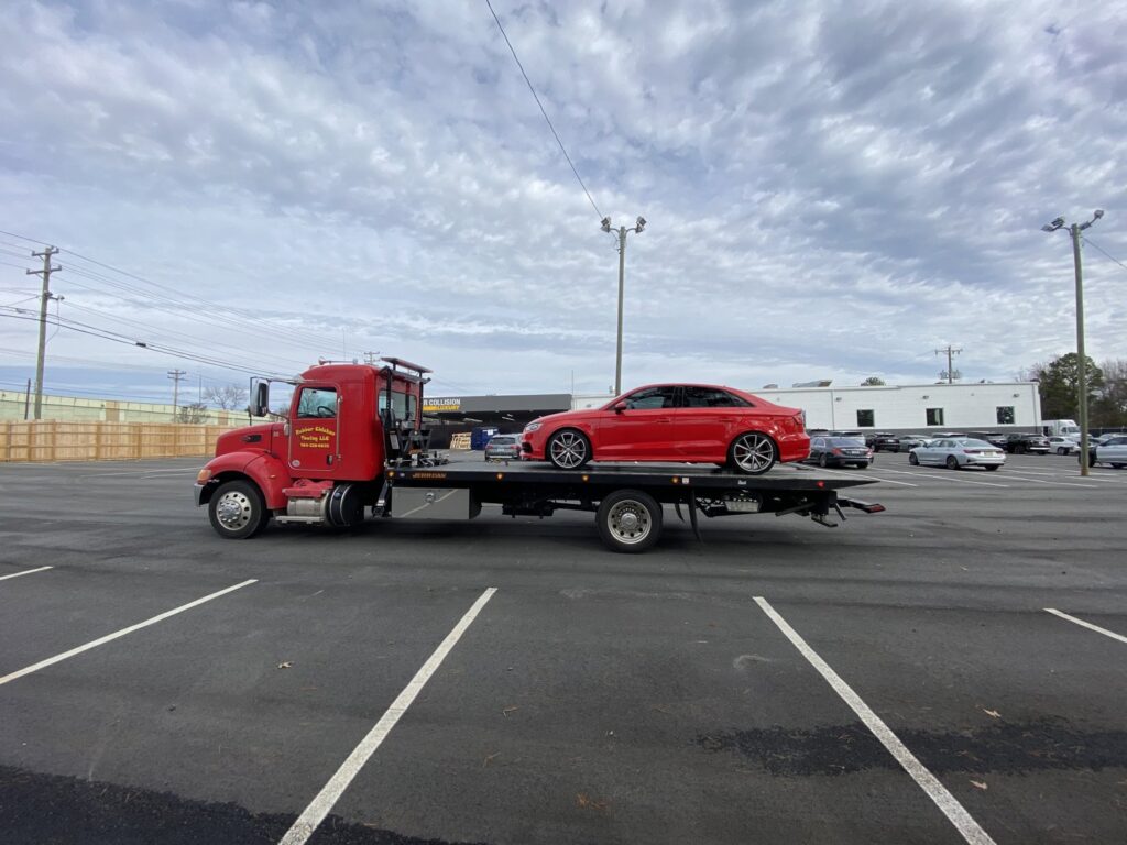 A red flatbed tow truck from Rubber Chicken Towing LLC towing a red sedan in a parking lot in Charlotte, NC.