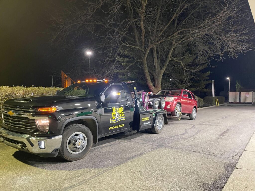 A Hound Dog's Towing & Recovery tow truck towing a red SUV at night in Columbus, OH.