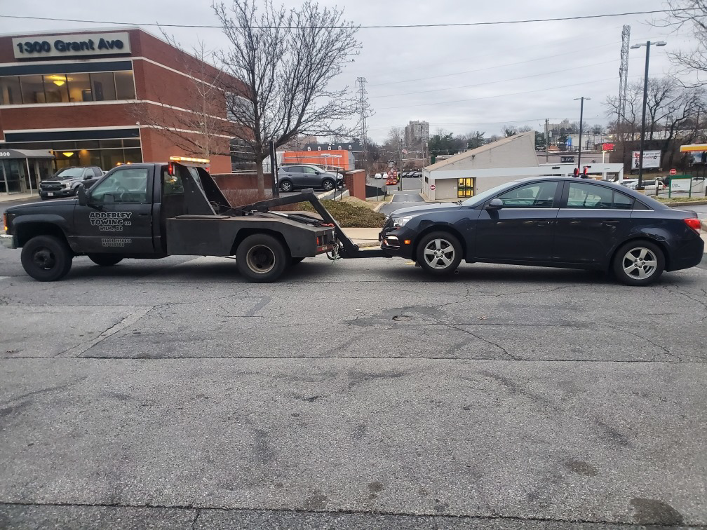 A tow truck from Adderley Towing LLC actively towing a dark sedan in Wilmington, DE.