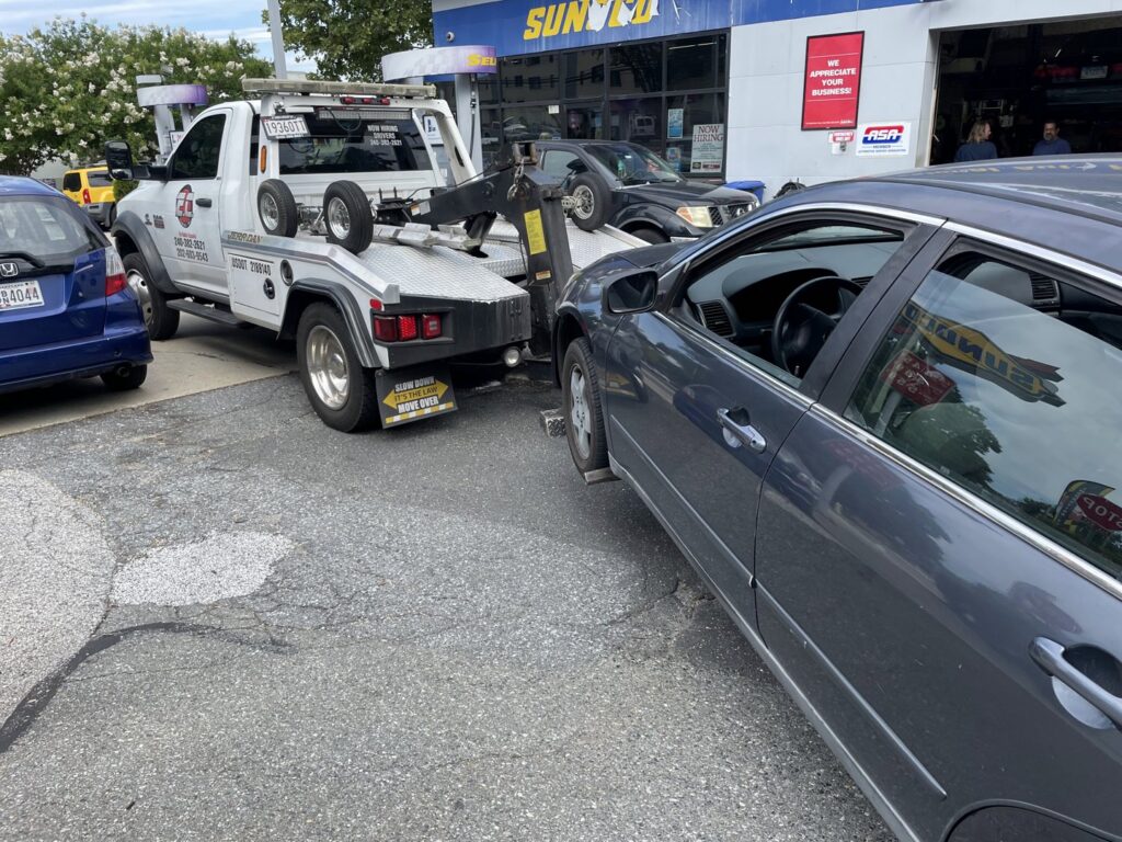 An E.C. Towing, Inc. tow truck towing a dark grey sedan from a gas station in Gaithersburg, MD.