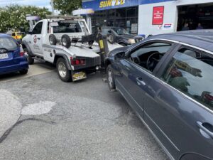 An E.C. Towing, Inc. tow truck towing a dark grey sedan from a gas station in Gaithersburg, MD.