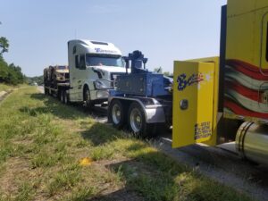 A Bevis Towing truck towing a semi-truck with military vehicles on a highway in Cincinnati, OH.