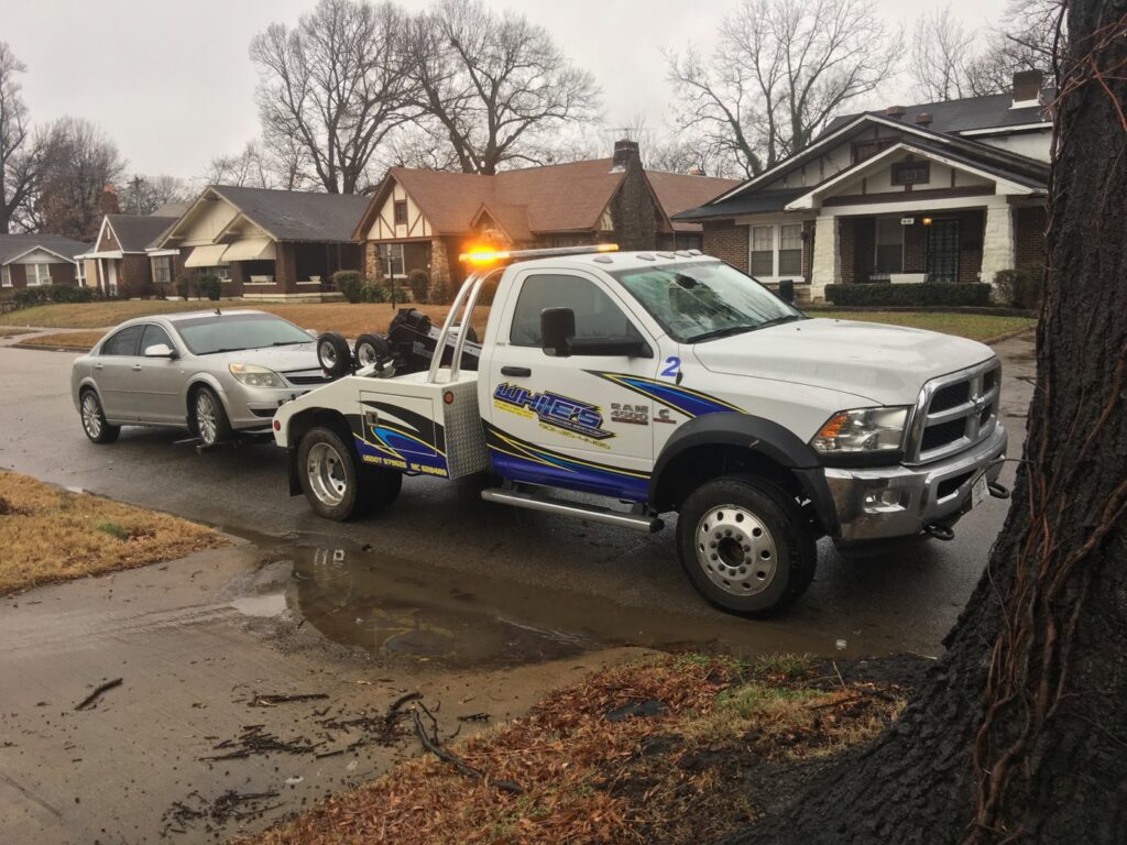 A White's Wrecker Service tow truck towing a silver car on a residential street in Memphis, TN.