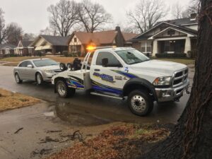A White's Wrecker Service tow truck towing a silver car on a residential street in Memphis, TN.