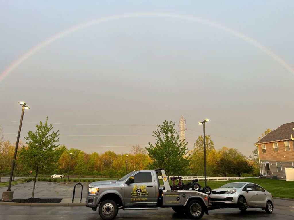 A Hound Dog's Towing & Recovery truck towing a silver car under a rainbow in Columbus, OH.