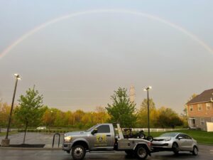 A Hound Dog's Towing & Recovery truck towing a silver car under a rainbow in Columbus, OH.