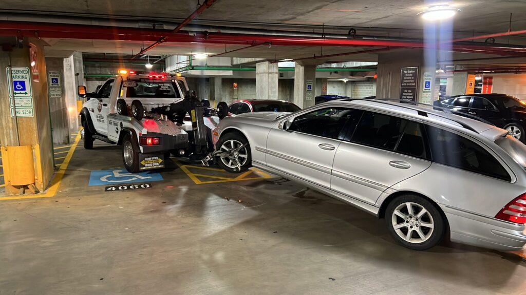 An E.C. Towing, Inc. tow truck towing a silver station wagon in an indoor parking garage in Gaithersburg, MD.