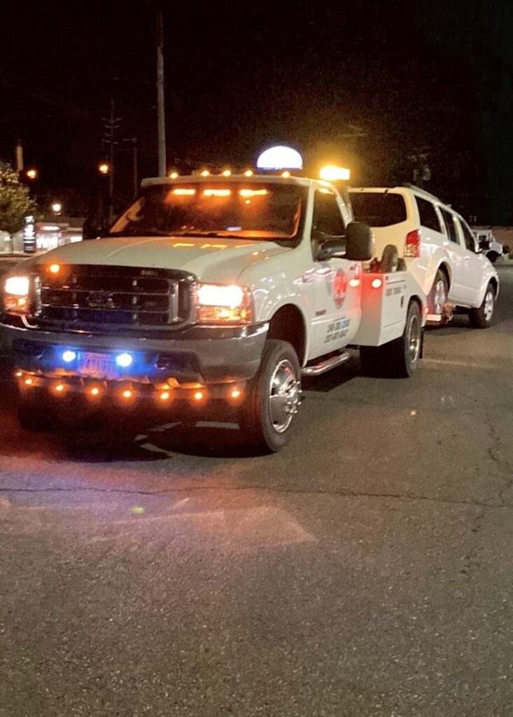 An E.C. Towing, Inc. tow truck towing a white SUV at night in Gaithersburg, MD.