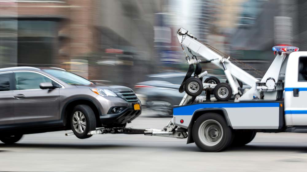 A professional tow truck actively towing a grey SUV on a city street for Towing Services Pittsburgh in Pittsburgh, PA.