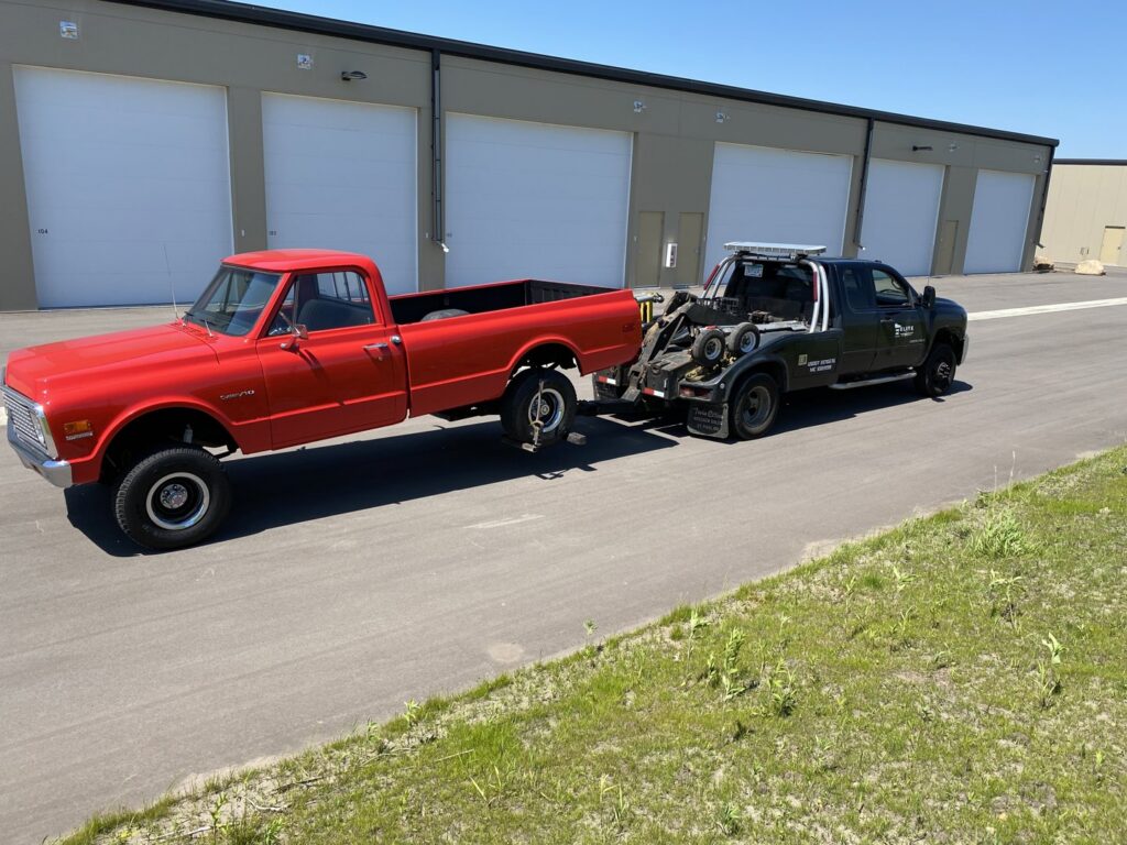 An Elite Towing of Minnesota tow truck towing a red vintage pickup truck by its front wheels in St Paul, MN.