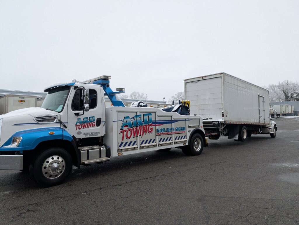 A white and blue A and D Towing truck is towing a white box truck on a cold day in Little Ferry, NJ.