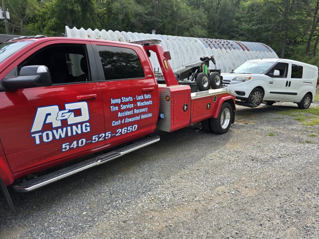 A red A and D Towing truck is towing a white cargo van on a gravel lot in Little Ferry, NJ.