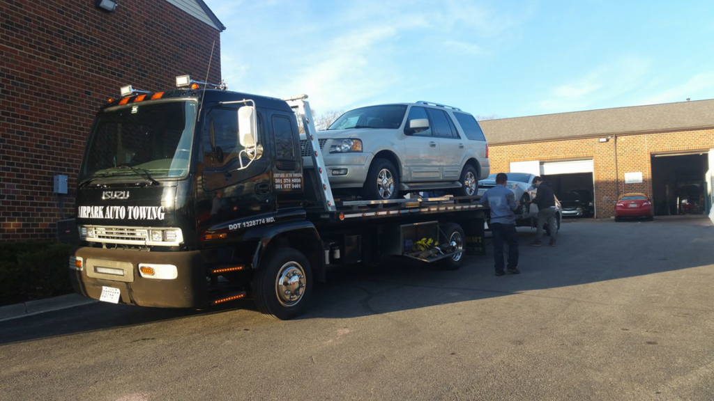 An Airpark Auto Center tow truck actively transporting a white SUV on its flatbed in Gaithersburg, MD.