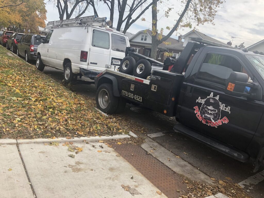 An O.T.W Towing & Recovery LLC tow truck preparing to tow a white van on a residential street in Chicago, IL.