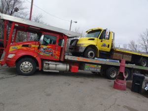 A red car carrier truck from Rivera Garcia Towing transporting a yellow flatbed tow truck in Omaha, NE.