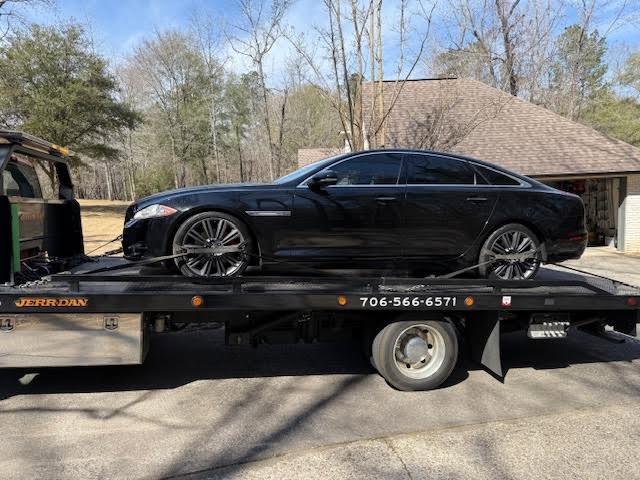 A tow truck from Advance Towing & Recovery transporting a black Jaguar sedan in Columbus, GA.