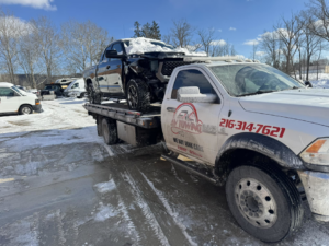 A tow truck from Av towing llc transporting a damaged black pickup truck in a snowy Cleveland, OH.