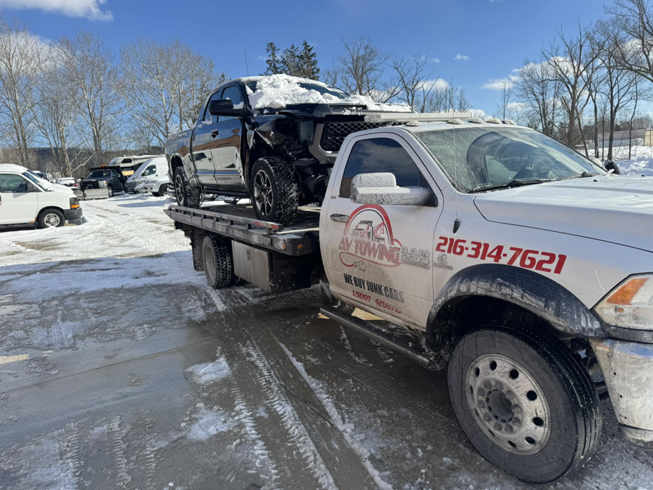 A tow truck from Av towing llc transporting a damaged black pickup truck in a snowy Cleveland, OH.