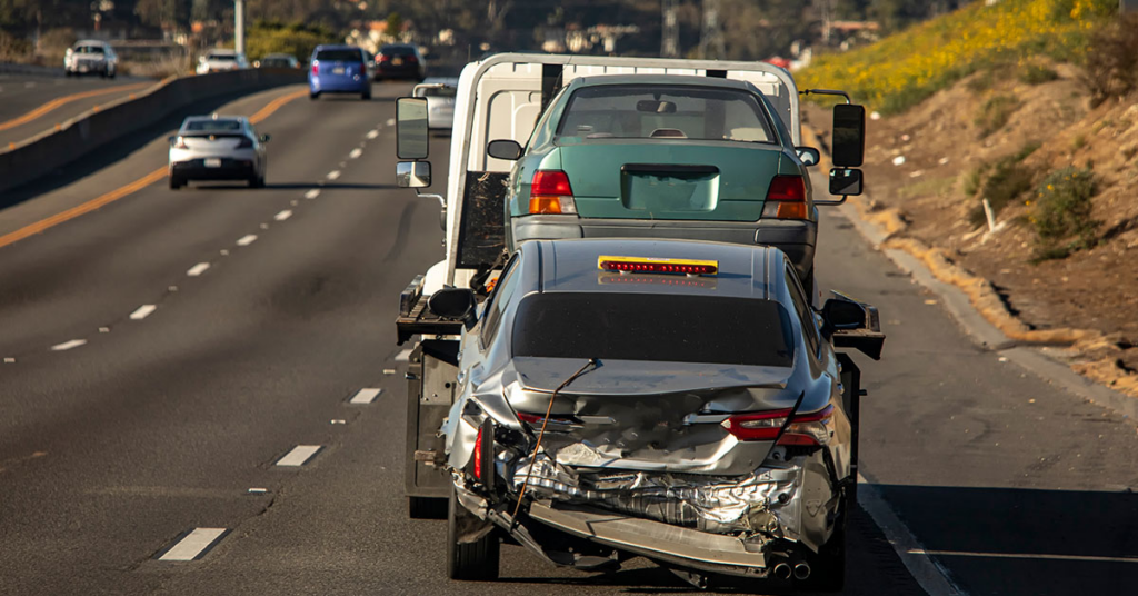 A tow truck transporting two vehicles, including a damaged car, on a highway for Atlantis Towing Services in Chicago, IL.