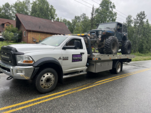 A Solid Choice Towing flatbed truck transporting a large off-road Jeep, providing reliable towing in Wasilla, AK.