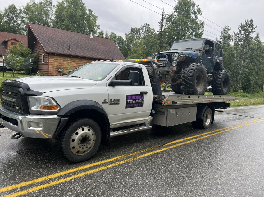A Solid Choice Towing flatbed truck transporting a large off-road Jeep, providing reliable towing in Wasilla, AK.
