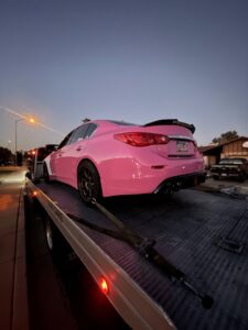 A C&B Towing flatbed truck transporting a custom pink sedan at dusk in Mesa, AZ.