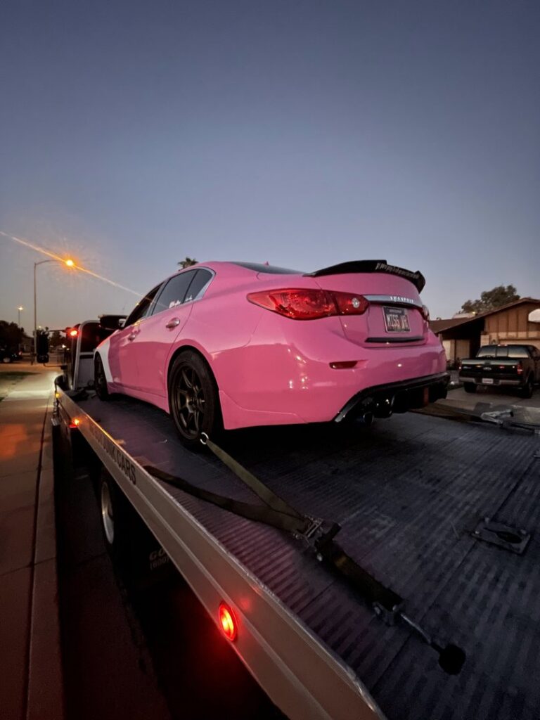A C&B Towing flatbed truck transporting a custom pink sedan at dusk in Mesa, AZ.