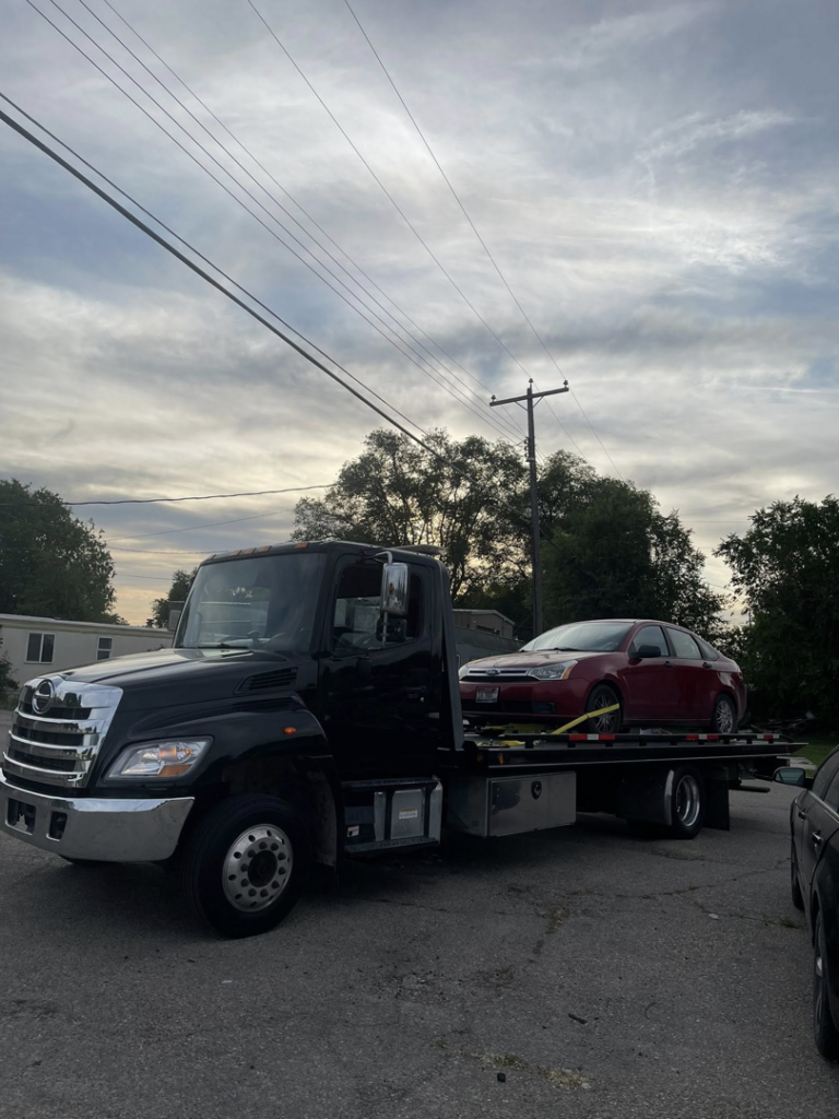 A black tow truck from A&R towing LLC transporting a red car on an overcast day in Nampa, ID.