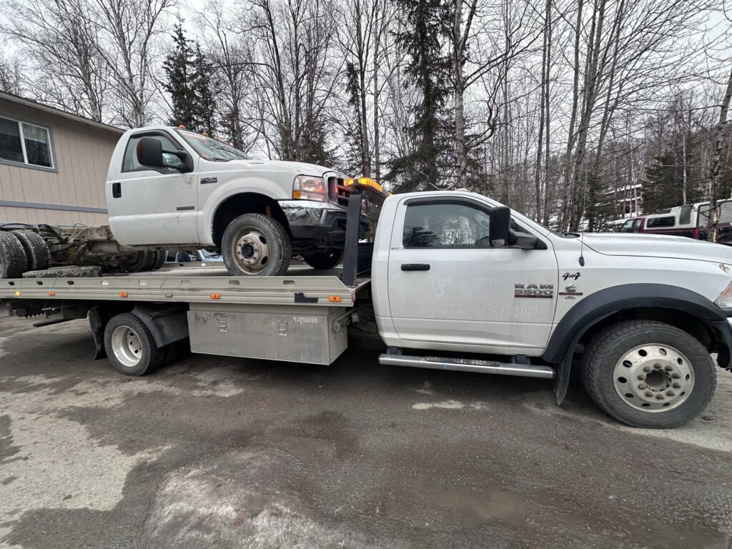 A Solid Choice Towing flatbed truck transporting a white truck cab, demonstrating specialized hauling in Wasilla, AK.