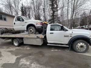 A Solid Choice Towing flatbed truck transporting a white truck cab, demonstrating specialized hauling in Wasilla, AK.