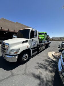 A C&B Towing flatbed truck transporting a vintage green pickup truck on a sunny day in Mesa, AZ.
