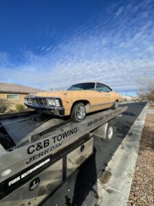 A C&B Towing flatbed truck transporting a vintage tan car on a residential street in Mesa, AZ.