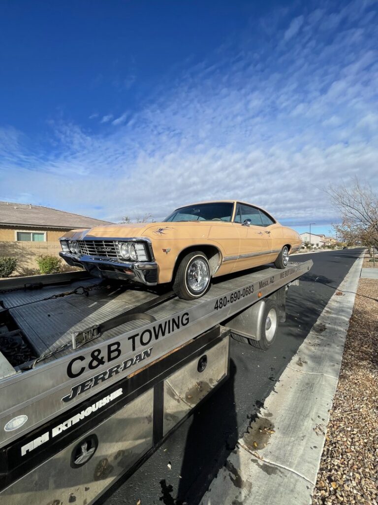 A C&B Towing flatbed truck transporting a vintage tan car on a residential street in Mesa, AZ.