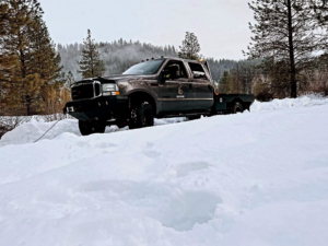 A tow truck with winch cable extended in snow, performing a recovery service by Mountain Goat Rescue & Recovery LLC + Towing in Nampa, ID.