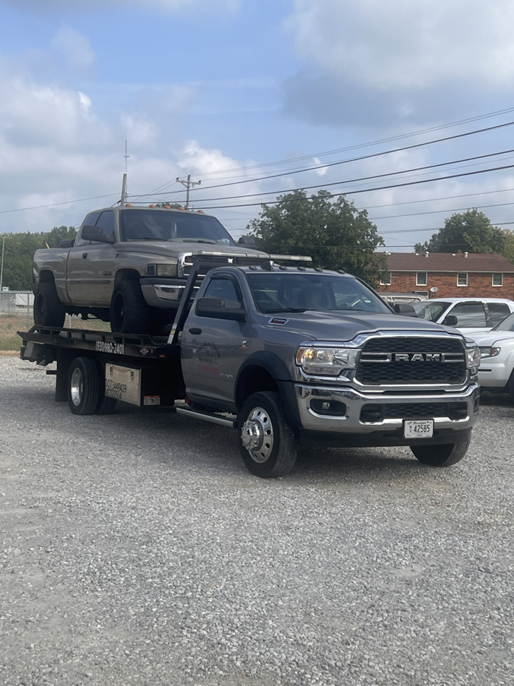 A gray RAM flatbed tow truck carrying a pickup truck at Two Guys Automotive Repair in Clarksville, TN