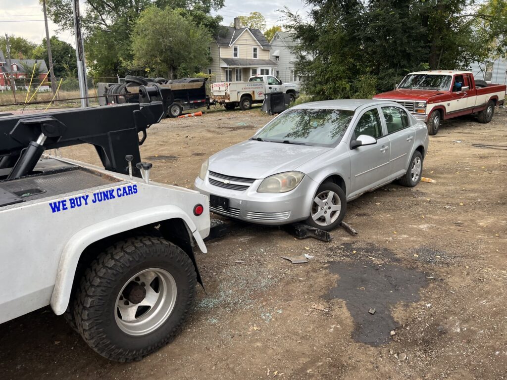 A tow truck from ALDM Management with a silver junk car in a lot, ready for removal in Cleveland, OH.