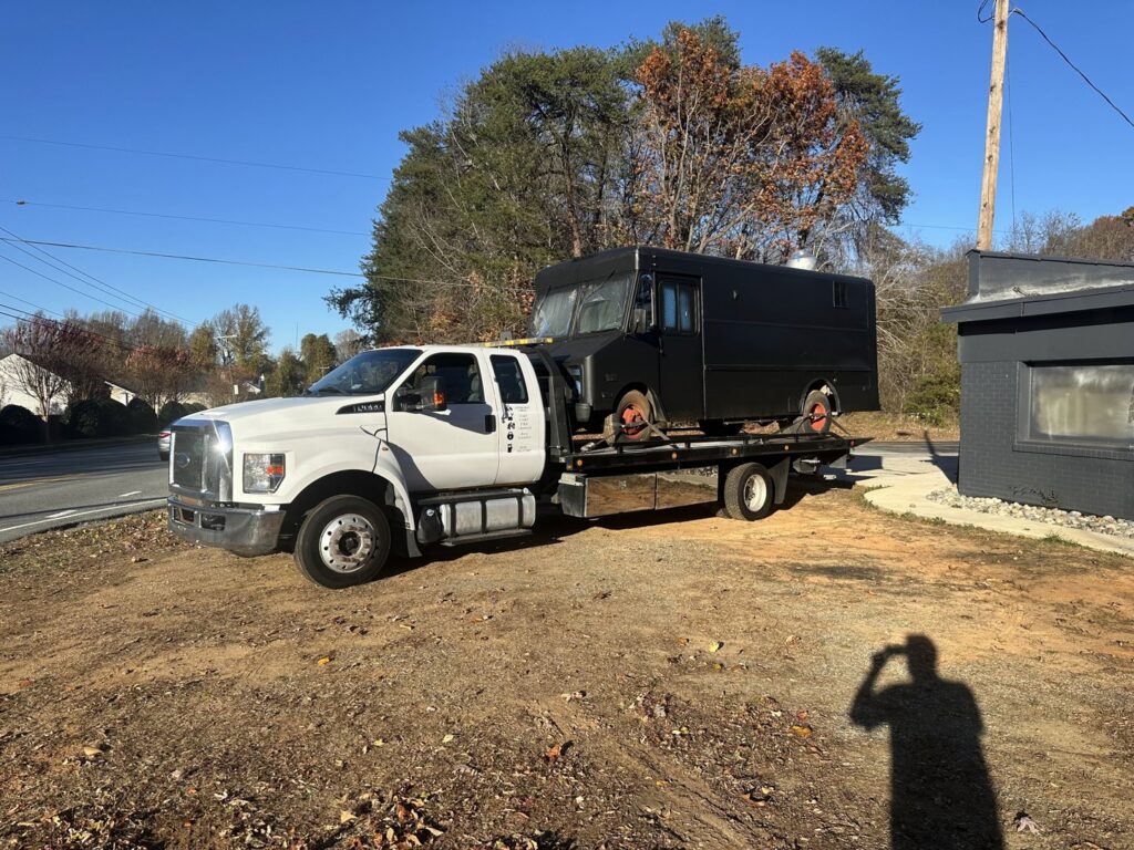 A Tow X flatbed tow truck transporting a black food truck in Greensboro, NC.