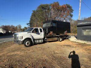 A Tow X flatbed tow truck transporting a black food truck in Greensboro, NC.