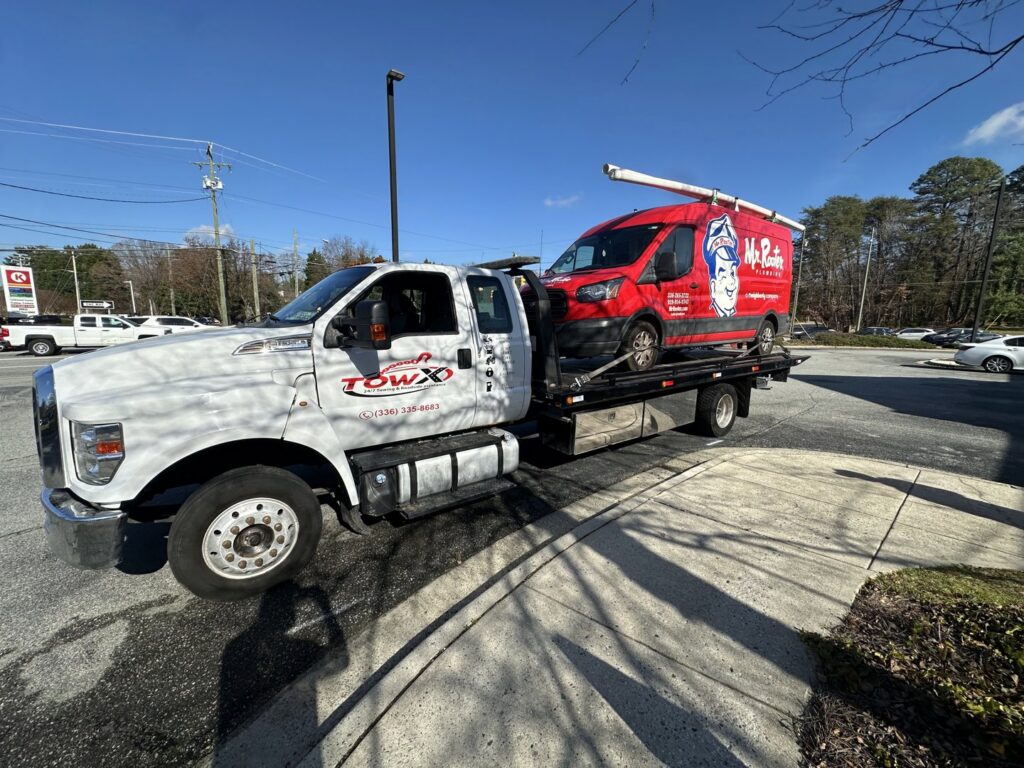A Tow X flatbed tow truck transporting a red van in Greensboro, NC.