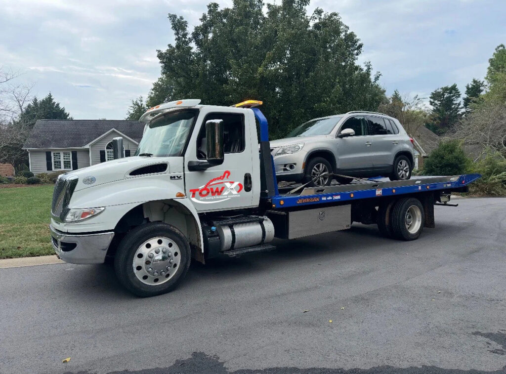 A Tow X flatbed tow truck transporting a silver SUV in a residential area in Greensboro, NC.